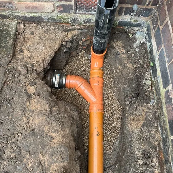 Newly installed orange PVC drainage pipes connected in an excavated trench next to a brick building